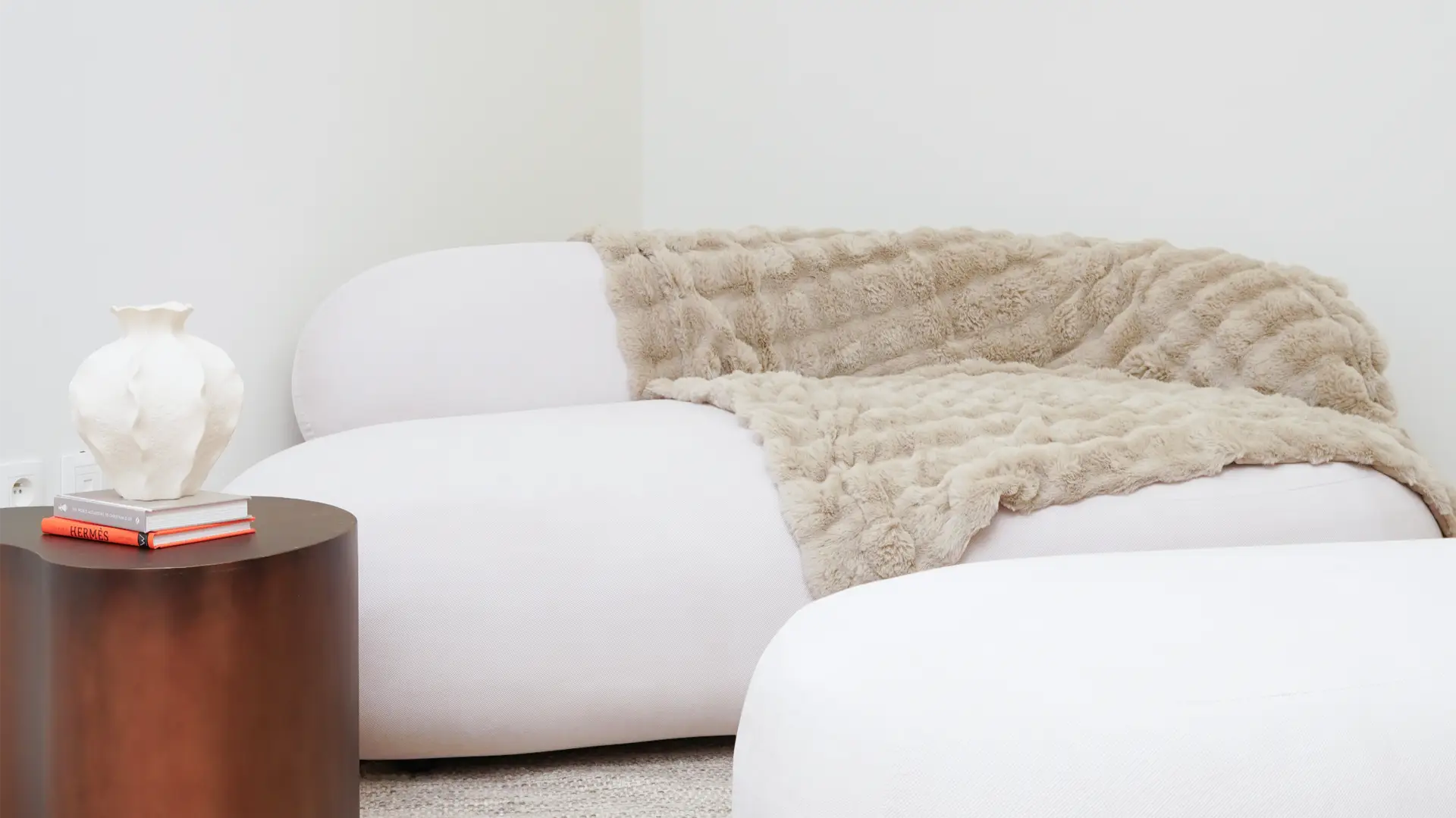 White sofa with fur blanket and wooden side table with decorative vase in Antwerp studio