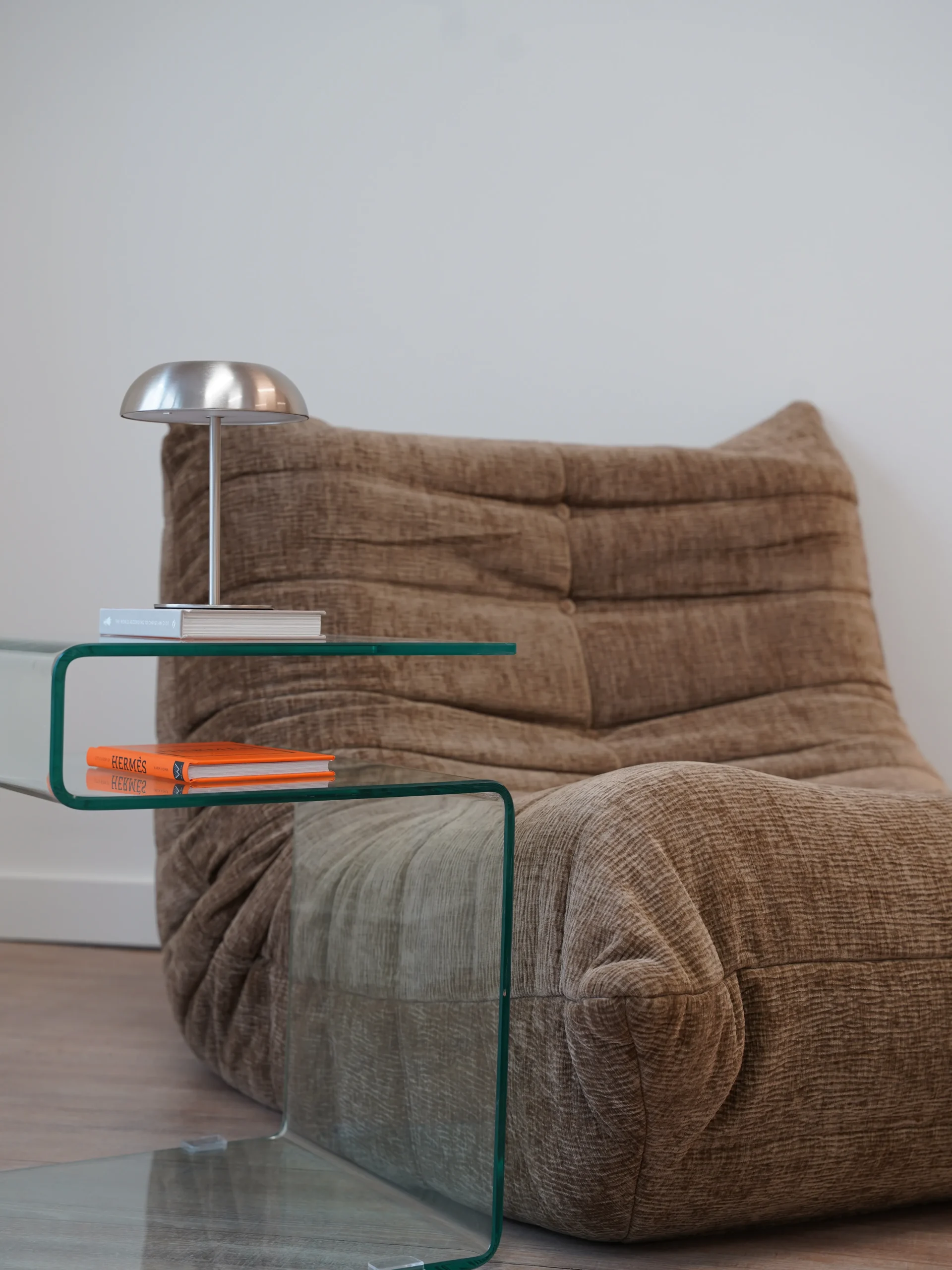 Brown lounge chair with glass side table, silver lamp, and books in Antwerp studio
