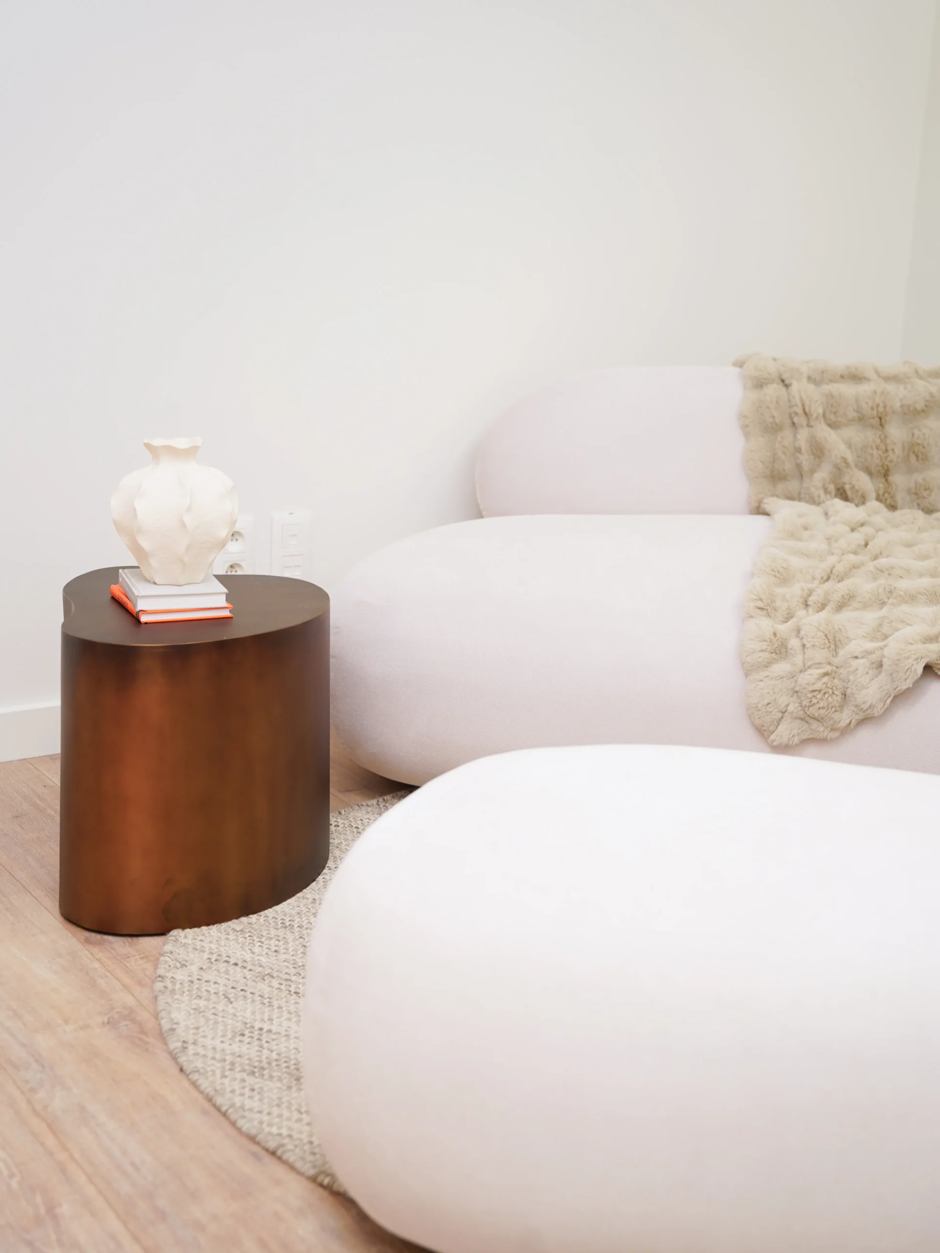 White sofa with fur blanket and vase on wooden side table in Antwerp studio