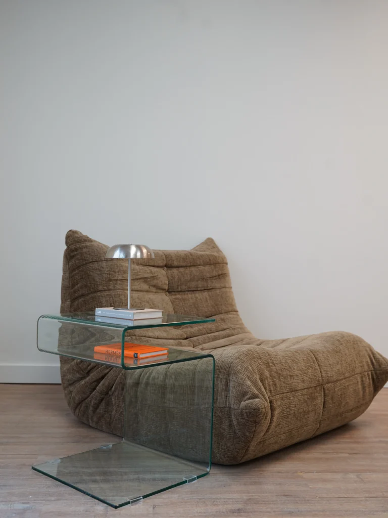 Brown lounge chair with glass side table, lamp, and stacked books in Antwerp studio