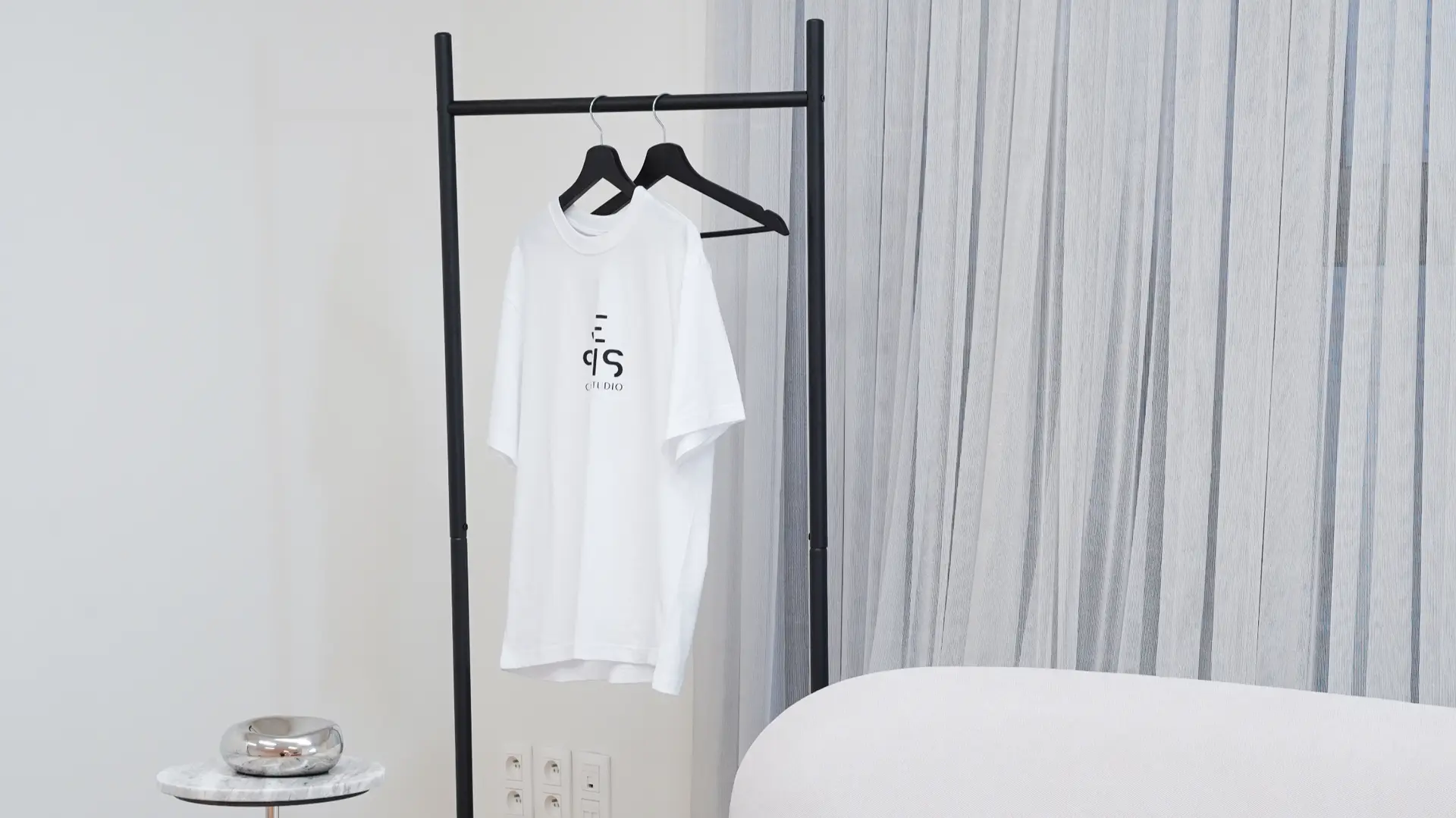 White Je Suis Content Studio branded t-shirt on clothing rack beside sofa in Antwerp